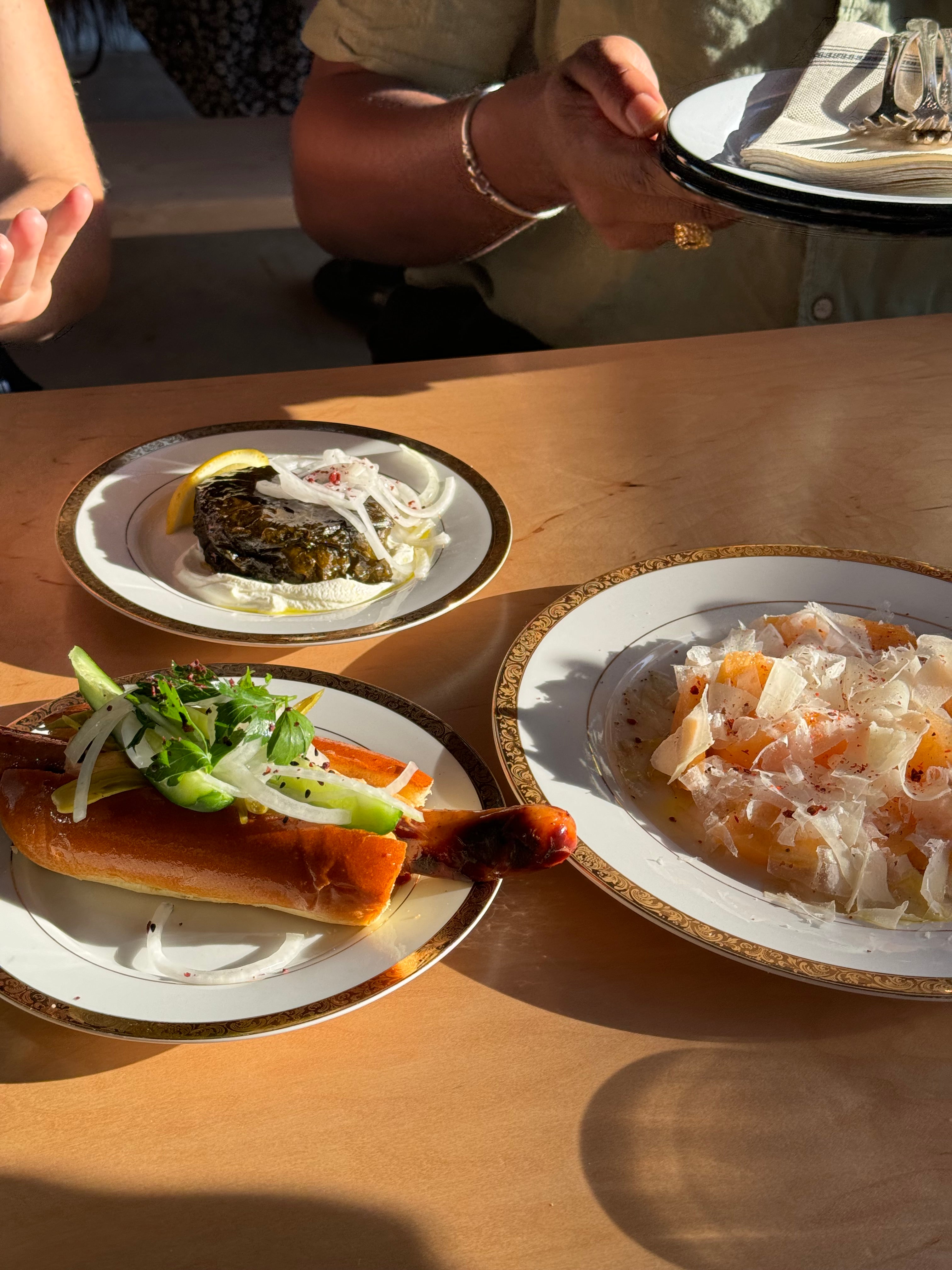 Plates of food on a wooden table with a person's hand holding a plate.
